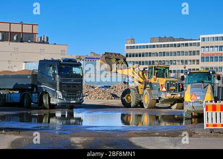 Komatsu Radlader Verladung Kies auf den Anhänger des schwarzen Volvo FH Kipper LKW auf der Baustelle an sonnigen Tag. Helsinki, Finnland. April 17, 2020 Stockfoto