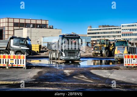 Schwarzer Volvo FH Kipper LKW mit einer Ladung Schotter verlässt Baustelle mit schweren Maschinen an sonnigen Tag. Helsinki, Finnland. 17. April 2020. Stockfoto