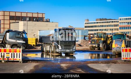 Schwarzer Volvo FH Kipper LKW mit einer Ladung Schotter verlässt Baustelle mit schweren Maschinen an sonnigen Tag. Helsinki, Finnland. 17. April 2020. Stockfoto