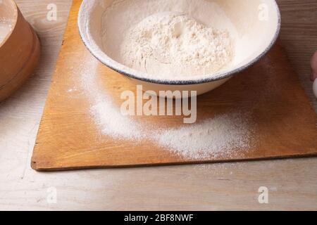 Große Schüssel, Schneidebrett, Sieb zum Sieben von Mehl auf dem Tisch. Weibliche Hände sieben Mehl in der Küche. Stockfoto