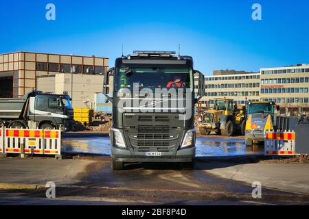 Schwarzer Volvo FH Kipper LKW mit einer Ladung Schotter verlässt Baustelle mit schweren Maschinen an sonnigen Tag. Helsinki, Finnland. 17. April 2020. Stockfoto