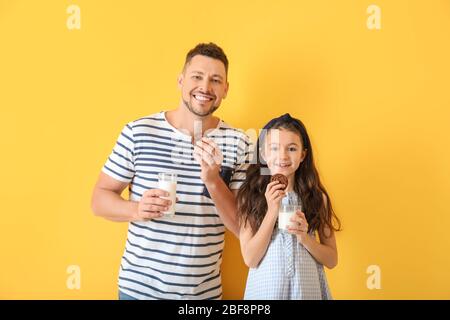 Vater und Tochter trinken Milch mit Cookies auf Farbhintergrund Stockfoto