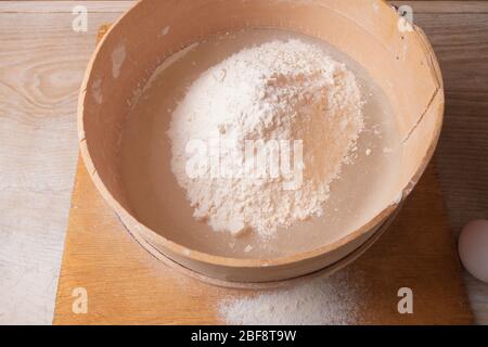 Große Schüssel, Schneidebrett, Sieb zum Sieben von Mehl auf dem Tisch. Weibliche Hände sieben Mehl in der Küche. Stockfoto