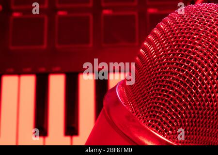 Nahaufnahme des Kondensator-Pro-Mikrofons mit Klaviertastatur im Hintergrund. Kopierbereich. Rotes Studio Stockfoto