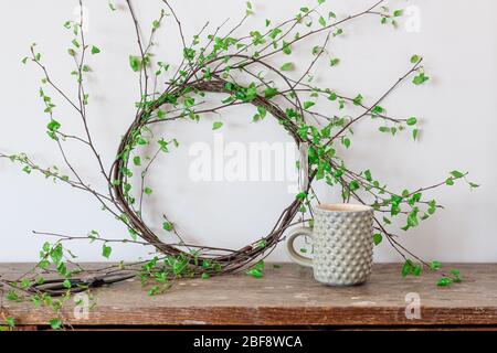 Grüner Birkenzweigen Kranz und eine Tasse Tee auf einem rustikalen Tisch Stockfoto