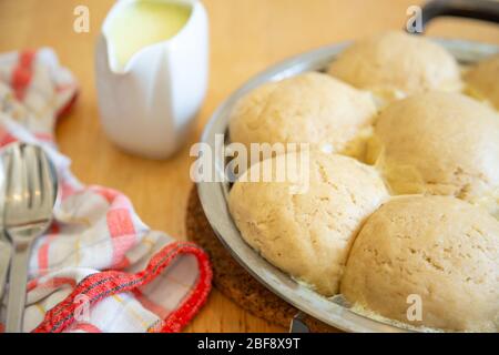 Traditionelle frische bayerische Hefeknödel, vegane Version, serviert mit Vanillesauce in einer Pfanne Stockfoto