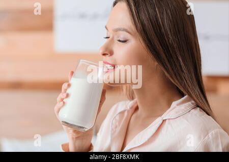 Junge Frau, die Milch im Schlafzimmer trinkt Stockfoto