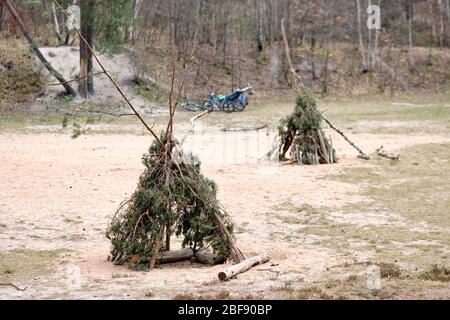 Zwei Teepis mit Zweigen und Zweigen von Nadelbäumen, die auf sandigen Grund im Wald stehen, mit Bycles im Hintergrund, die man in Deutschland im April gesehen hat. Stockfoto