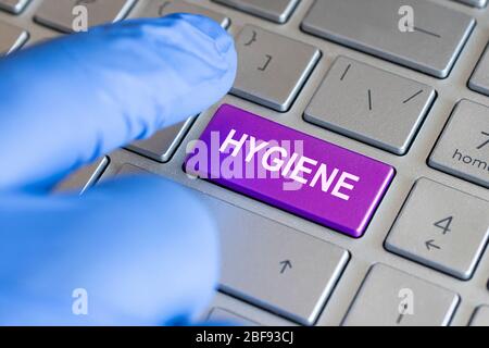 Hygiene-Wort auf der Tastatur-Taste, Schutz vor Keimen. Ein Finger in einem blauen medizinischen Handschuh drückt eine farbige Taste auf dem Laptop. Stockfoto