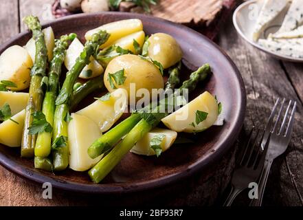 Gekochte Kartoffel mit gegrilltem grünen Spargel auf braunem Teller auf altem Holzhintergrund. Stockfoto