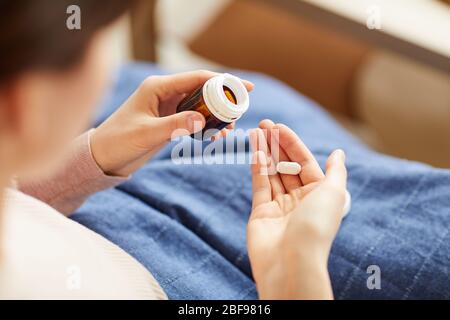 Nahaufnahme einer Frau, die eine Pille oder ein Vitamin nimmt, während sie zu Hause auf dem Bett liegt Stockfoto