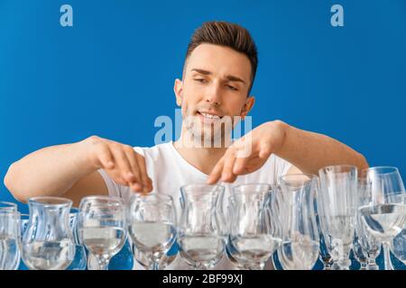 Junger Mann spielt Musik auf Gläsern mit Wasser vor farbigen Hintergrund Stockfoto