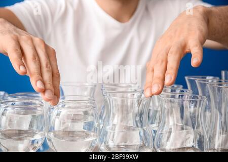 Junger Mann spielt Musik auf Gläsern mit Wasser vor Farbhintergrund, Nahaufnahme Stockfoto
