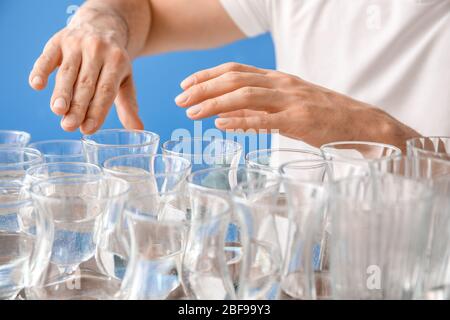 Junger Mann spielt Musik auf Gläsern mit Wasser vor Farbhintergrund, Nahaufnahme Stockfoto