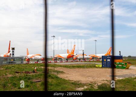Southend-on-Sea, Großbritannien. April 2020. Eine Reihe von EasyJet-Flugzeugen in orange-weißer Lackierung, die auf dem Asphalt am Flughafen London Southend geparkt sind und durch einen Drahtzaun gesehen werden. Sichtbare Baumaschinen und Barrieren deuten auf eine Wartungs- oder Lagerzone innerhalb des eingeschränkten luftseitigen Bereichs hin. Nach Maßnahmen, die von europäischen Staaten und großen europäischen Fluggesellschaften als Reaktion auf die COVID-19-Pandemie ergriffen wurden, sitzen die easyJet-Flugzeuge auf der Start- und Landebahn des Flughafens Southend. Penelope Barritt/Alamy Live News Stockfoto