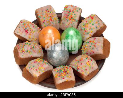 Mini-Osterkuchen mit Zuckerguss und bunten Zuckerstreuseln und drei farbigen Eiern in einem Teller Stockfoto