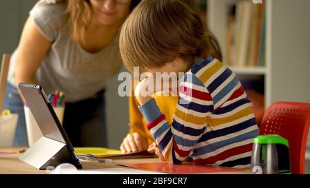 Fernunterricht von Schulfächern für Tochter und Sohn zu Hause. Mutter steuert den Prozess der Hausaufgaben für Tochter und Sohn auf einem Laptop. Stockfoto