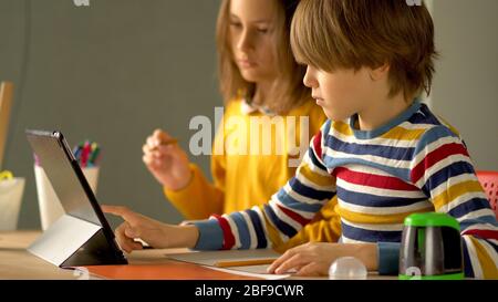 Fernunterricht von Schulfächern für Tochter und Sohn zu Hause. Mutter steuert den Prozess der Hausaufgaben für Tochter und Sohn auf einem Laptop. Stockfoto