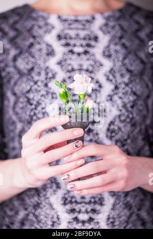 Weibliche Hände mit rosa Nelkenblüten in schwarzen Waffelkegel auf einem schwarz-weißen Kleid. Struktur aus Schlangenhaut Stockfoto