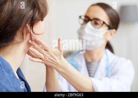 Junge Frau sitzt, während die Krankenschwester ihren Hals während des Besuchs im Krankenhaus untersucht Stockfoto