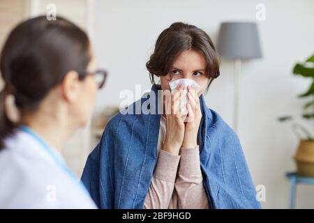 Kranke junge Frau sitzt mit Arzt und spricht mit ihr über die Krankheit im Wohnzimmer zu Hause Stockfoto