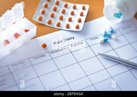 Schmerzbehandlung Konzept: Wöchentliche Schmerztabellenblatt für Ursachenanalyse mit Stift und Medizin. Stockfoto