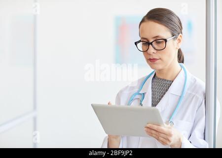 Junge Ärztin in Brillen mit weißem Fell und mit digitalem Tablet im Krankenhaus Stockfoto