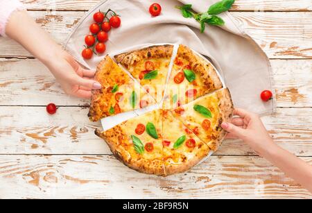 Leute, die Scheiben von köstlicher Pizza Margherita vom Tisch nehmen Stockfoto