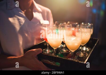 Die Kellnerin trägt ein Tablett mit Softdrink-Willkommensdrink-Brille, um neue Gäste in einem Hotel mit Party-Nughtclub und Restaurant willkommen zu heißen. Das Nachtleben ist prickelnd Stockfoto