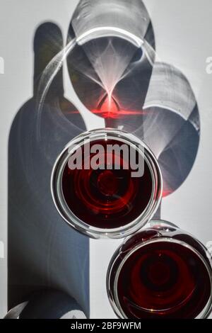 Nahaufnahme von Gläsern Rotwein und Korkenzieher mit Schatten und Reflexen auf einer weißen strukturierten Oberfläche. Stockfoto