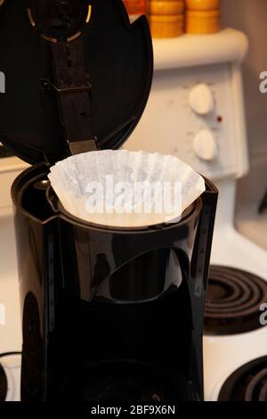 Ein weißer Papierfilter sitzt in der Oberseite einer Tropfkaffeemaschine auf dem Herd Stockfoto