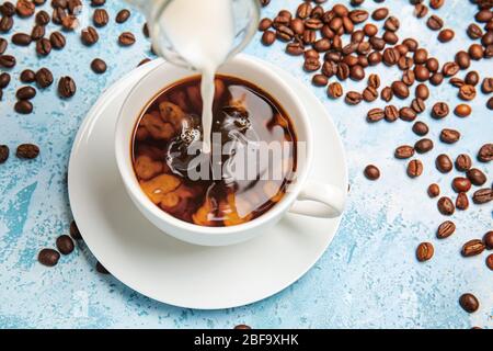Gießen von Milch in einer Tasse heißen Kaffee auf dem Tisch Stockfoto