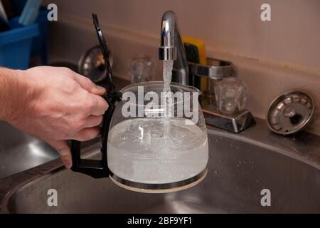 Füllen Sie die Glaskaffeekanne mit Wasser in der Spüle Stockfoto