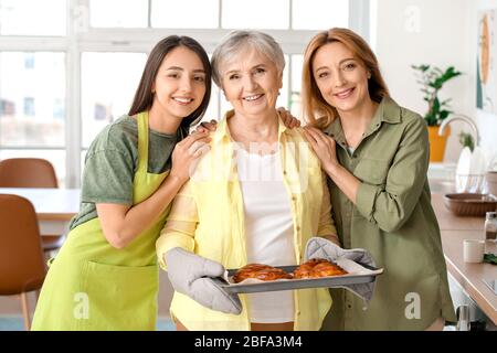 Reife Frau mit ihrer erwachsenen Tochter und Mutter kochen Brötchen zusammen zu Hause Stockfoto