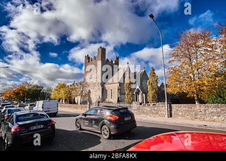 Straßenansicht der Heiligen Dreifaltigkeit Abteikirche, Adare, Co. Limerick im Oktober Herbst mit Autos fahren auf verkehrsreichen Straße Stockfoto