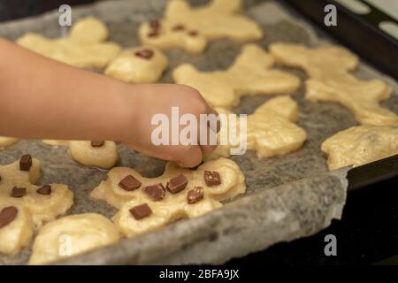 Eine Kinderhand schmückt Schokoladenstücke mit hausgemachten Keksen auf einem Backblech. Aktivitäten mit Kindern in der Quarantänezeit zu Hause Stockfoto