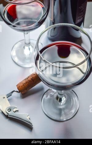 Nahaufnahme von Gläsern Rotwein und Korkenzieher mit Schatten und Reflexen auf einer weißen strukturierten Oberfläche. Stockfoto