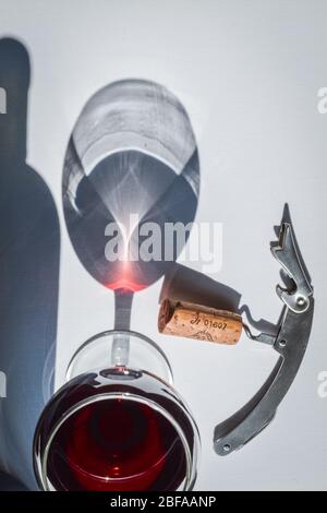 Nahaufnahme von Gläsern Rotwein und Korkenzieher mit Schatten und Reflexen auf einer weißen strukturierten Oberfläche. Stockfoto