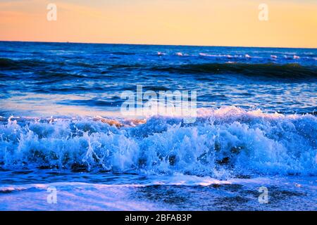 Toller Sonnenuntergang am Strand mit unglaublich glitzernden Wellen. Sonnenuntergang und Wellen am spektakulären Strand. Blau und Gelb unendlich Stockfoto