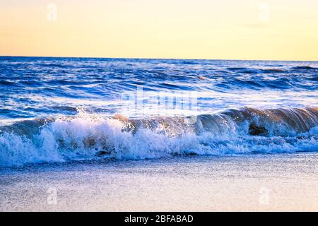 Toller Sonnenuntergang am Strand mit unglaublich glitzernden Wellen. Sonnenuntergang und Wellen am spektakulären Strand. Blau und Gelb unendlich Stockfoto