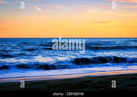 Toller Sonnenuntergang am Strand mit unglaublich glitzernden Wellen. Sonnenuntergang und Wellen am spektakulären Strand. Blau und Gelb unendlich Stockfoto