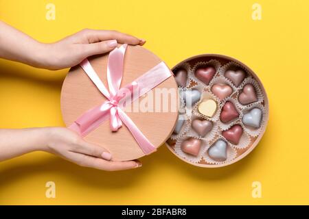 Weibliche Hände mit köstlichen Süßigkeiten in Box auf Farbhintergrund Stockfoto
