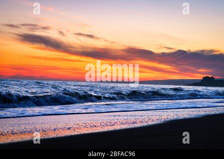 Toller Sonnenuntergang am Strand mit unglaublich glitzernden Wellen. Sonnenuntergang und Wellen am spektakulären Strand. Blau und Gelb unendlich Stockfoto