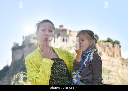 Nette kleine vorschulische Mädchen und junge Mutter Blick auf Kamera weht einen Kuss. Mutter und Tochter reisen zusammen in einem wunderschönen Reiseziel in Italien. Stockfoto