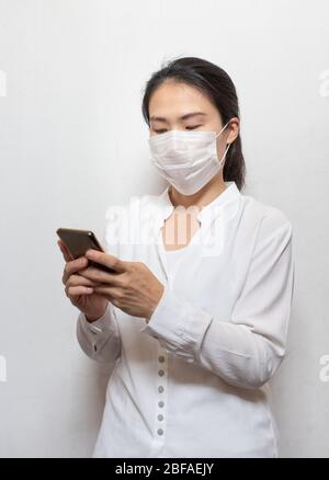 Junge asiatische Frau trägt chirurgische Maske verhindern, dass mit Smartphone isoliert auf weißem Hintergrund, Wuhan Coronavirus (COVID-19) Ausbruch Prävention Stockfoto