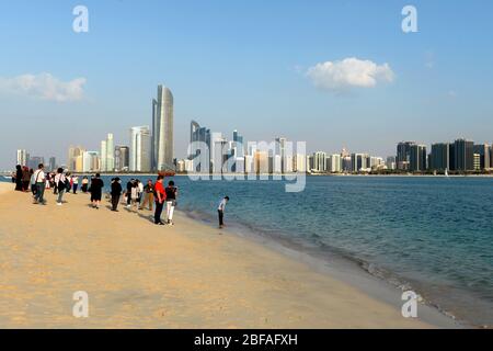 Touristen posieren für Fotos mit Abu Dhabi Skyline mit mehreren Wolkenkratzern dahinter. Beliebte Sehenswürdigkeiten für Reisende in Vereinigte Arabische Emirate. Stockfoto