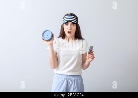 Beunruhigte Frau mit Schlafpillen und Uhr auf hellem Hintergrund Stockfoto