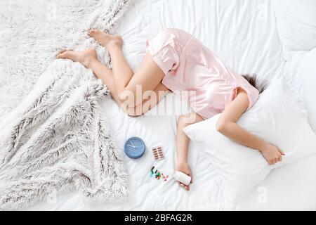 Junge Frau mit Pillen für Schlaflosigkeit und Uhr schlafen im Bett Stockfoto