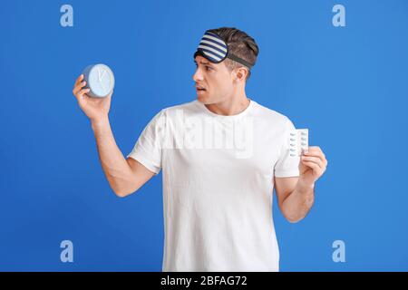 Beunruhigte Mann mit Schlafpillen und Uhr auf farbigen Hintergrund Stockfoto