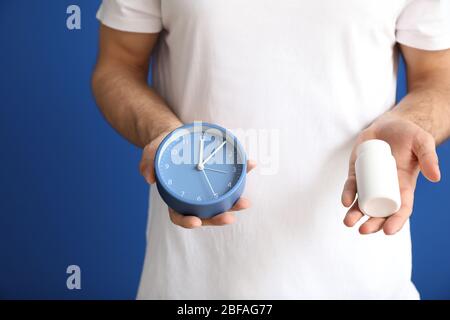 Junger Mann mit Schlafpillen und Uhr auf farbigem Hintergrund, Nahaufnahme Stockfoto